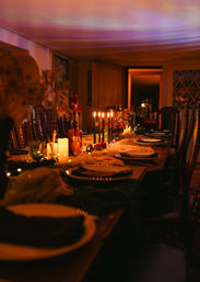 Candlelit long dining table in a cozy dining room, elegant place settings and autumn centerpiece under warm amber lighting.