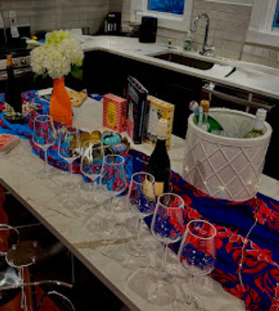 Party-ready modern kitchen island with rows of wine glasses, champagne bottles in an ice bucket, colorful streamers, and a white flower bouquet on the countertop.