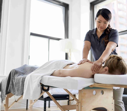 Massage therapist giving a back and neck massage to a client lying face down on a massage table in a bright urban wellness studio