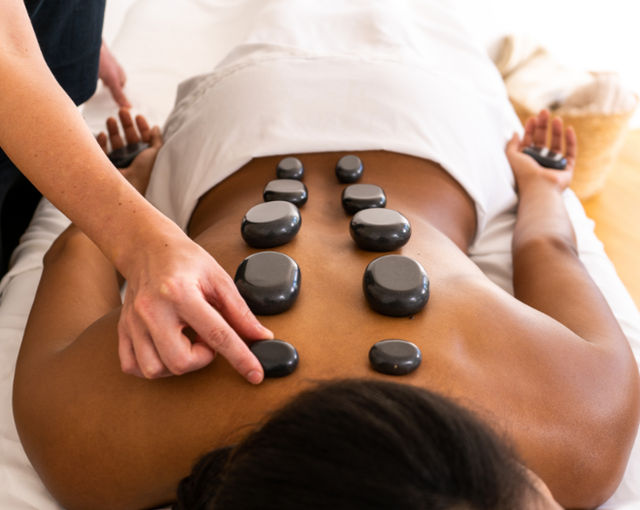 Hot stone spa massage with smooth black basalt stones aligned along a client's bare back as a therapist places one for relaxation