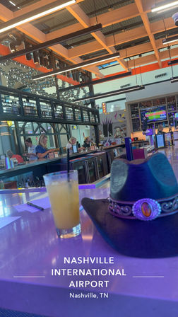 Nashville International Airport terminal bar with illuminated counter, a cocktail with straw and a cowboy hat on the bar, patrons, TVs and modern wood-grid ceiling