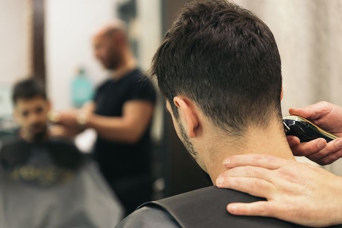 Barber trimming a man's neckline with electric clippers at a modern barbershop, haircut in progress