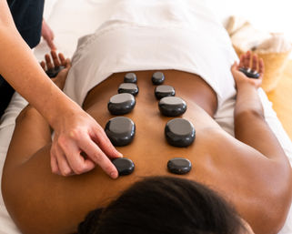 Hot stone back massage at a spa: smooth black stones arranged along the spine as a therapist places a stone for relaxation