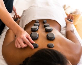 Client receiving hot stone massage with smooth black stones placed along the spine on a massage table in a relaxing spa setting