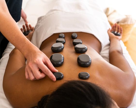 Client receiving hot stone massage with smooth black stones placed along the spine on a massage table in a relaxing spa setting