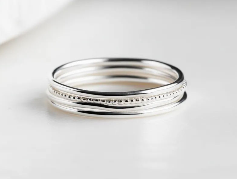 Close-up of three sterling silver stacking rings — smooth and beaded bands on a clean white background, minimalist jewelry product photo.