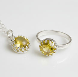 Close-up studio photo of a silver ring and matching pendant with round faceted yellow gemstone set in decorative crown-style prongs on a white background