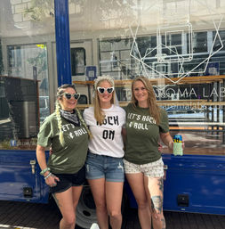 Three smiling women posing on a city sidewalk in front of a blue food truck — bachelorette in center with veil and heart sunglasses, friends in matching 'Let’s Rock & Roll' shirts.