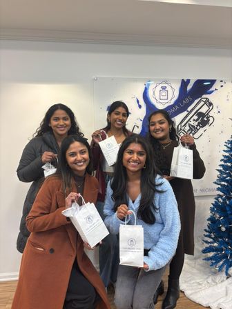 Group of five smiling women in a boutique gift shop holding white shopping bags, posing beside a blue holiday tree and colorful wall art.