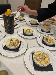 Plated mini mushroom and cheese quiches in white ramekins on decorative plates with black napkins, hand drizzling extra virgin olive oil — catered appetizer spread.
