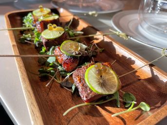 Zesty glazed meat bites on skewers topped with thin lime slices and citrus pearls, served on microgreens on a wooden platter — restaurant appetizer