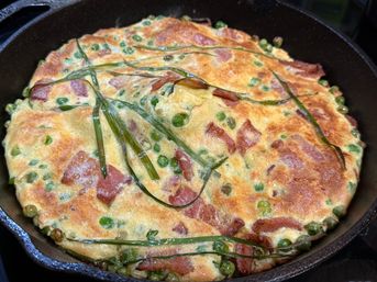 Golden-brown frittata in a cast-iron skillet with peas, diced ham and chive ribbons — a savory brunch-ready skillet dish