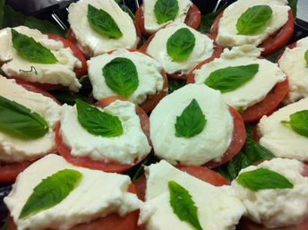 Close-up of Caprese-style appetizer: juicy tomato rounds topped with creamy fresh mozzarella and bright green basil leaves arranged on a platter