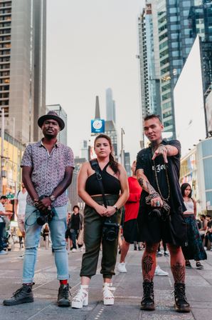 Three street photographers posing in Times Square, New York City — a diverse trio with cameras against a backdrop of skyscrapers and bright billboards.