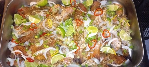 Tray of whole spiced fried fish garnished with lime wedges, sliced onions, scallions and red and yellow chili rings — zesty seafood platter.