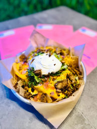 Parchment-lined metal bowl of loaded nachos with melted cheddar, grilled chicken, pico de gallo, shredded lettuce and a dollop of sour cream