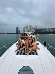 Group of friends lounging and waving on the bow of a white yacht with the Chicago skyline and Navy Pier Ferris wheel across Lake Michigan under a cloudy sky