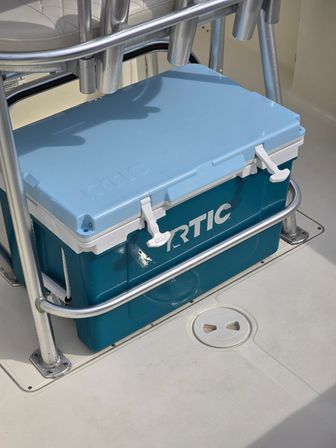 Teal and light-blue hard cooler tucked under stainless-steel seat rail on a white boat deck