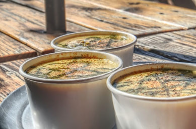 Three paper cups of creamy spiced soup with herb drizzle on a rustic wooden outdoor table