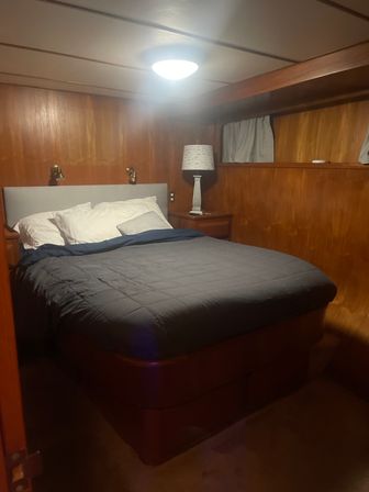 Cozy wood-paneled cabin bedroom with a raised queen bed dressed in a gray comforter and white pillows, brass reading sconces above the headboard, and a bedside lamp — warm, compact sleeping space.