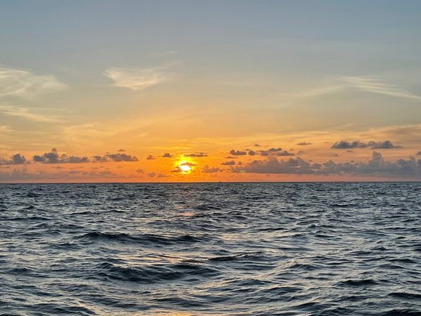 Vibrant orange and gold sunset over the open ocean, sun dipping at the horizon with rippling waves and scattered clouds