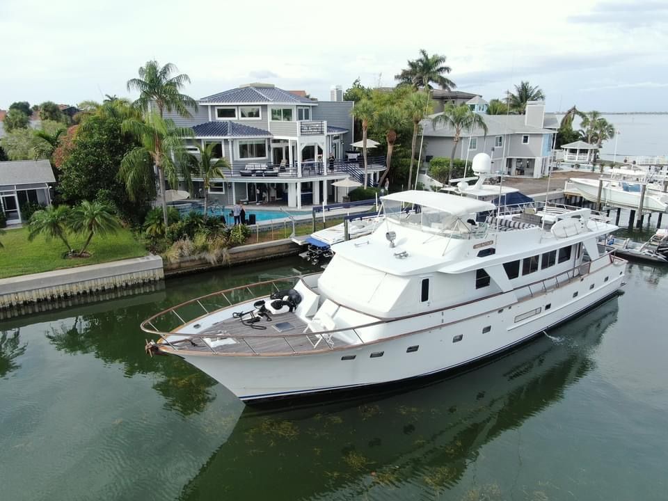 White luxury motor yacht gliding through a calm residential canal past waterfront multi‑story homes with palm trees, private docks and a backyard pool