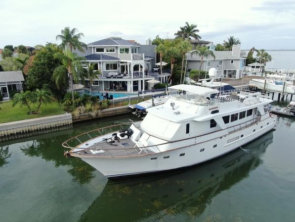 White luxury motor yacht gliding through a calm residential canal past waterfront multi‑story homes with palm trees, private docks and a backyard pool