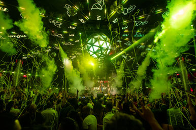 Packed nightclub dance floor with DJ on stage, vivid green lasers and smoke, geometric LED disco ball, and streamers raining down on a cheering crowd.