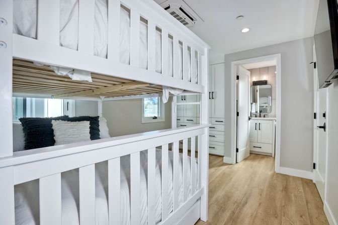 Bright modern bedroom featuring a white wooden bunk bed, wood-look flooring, built-in white cabinetry and a small ensuite bathroom with vanity — airy kids/guest room.