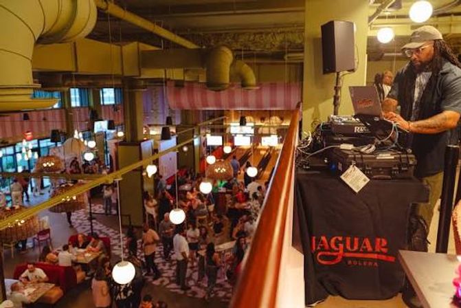 Mezzanine DJ spinning over a lively indoor bowling alley and lounge with hanging globe lights and crowds