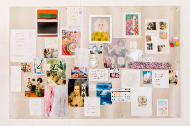 Vibrant mood board on a striped pinboard in a creative studio — photos, art prints, postcards, sketches and colorful collages.