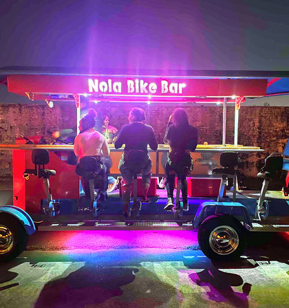 Group pedaling at a neon-lit mobile pedal bar on a New Orleans street at night, colorful lights reflecting on pavement.