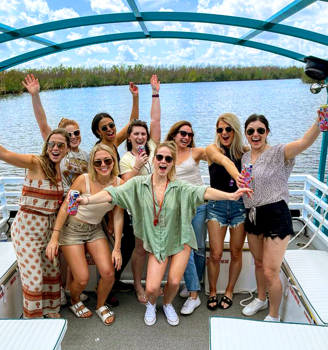 Group of friends cheering on a pontoon boat over a sunny lake, wearing sunglasses and holding colorful drinks — summer boat outing.