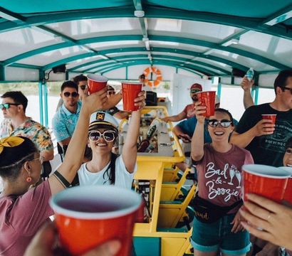 Group of friends on a covered party boat raising red cups in a cheerful toast during a sunny lake cruise