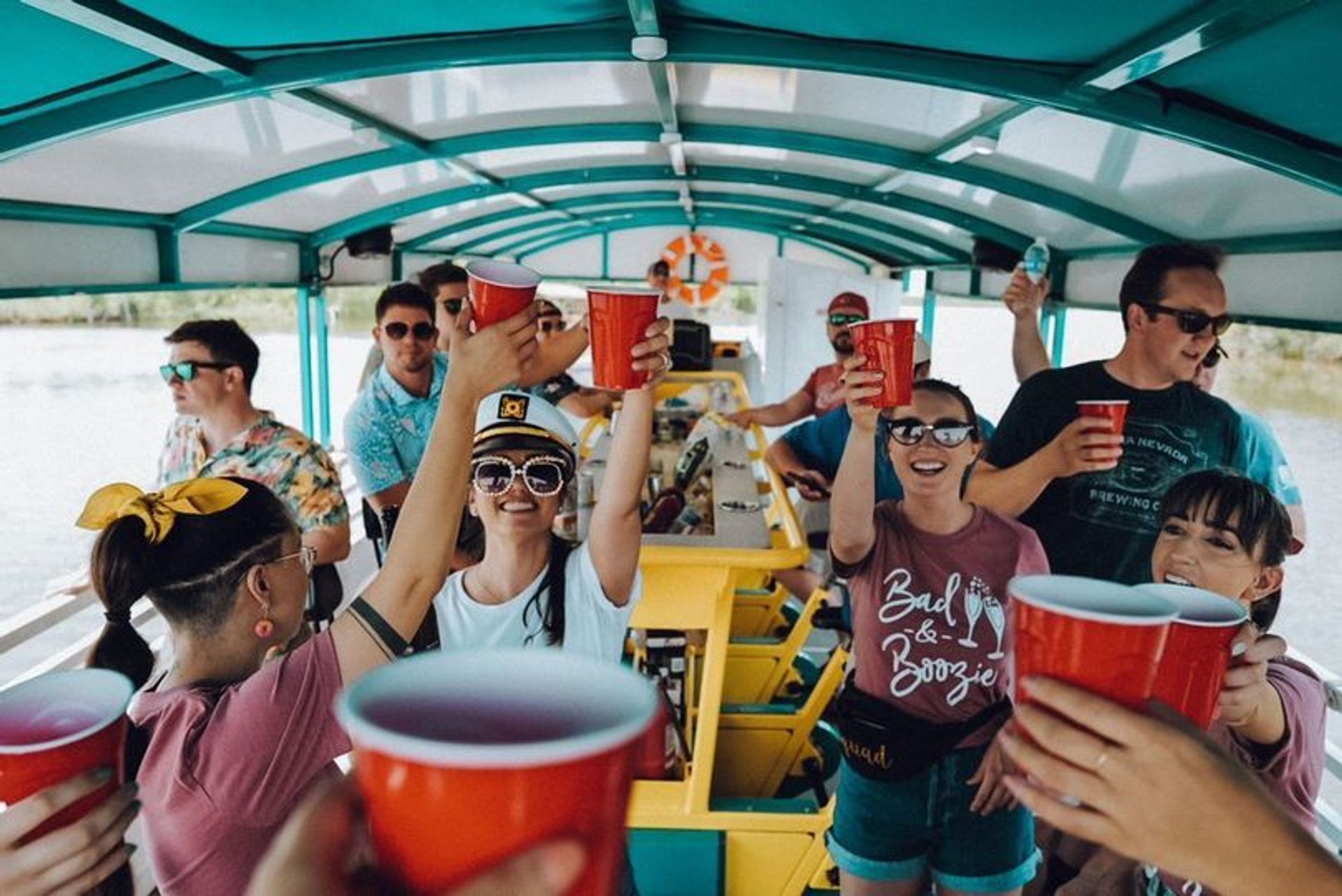Group of friends on a covered party boat raising red cups in a cheerful toast during a sunny lake cruise