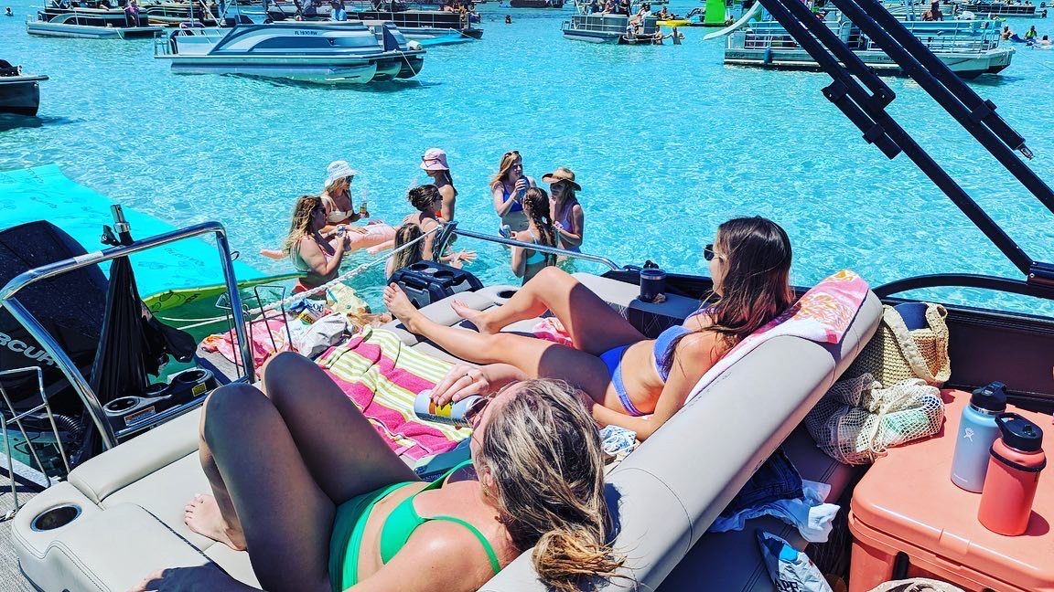 Summer boat party: people sunbathing on a pontoon with anchored boats and swimmers in crystal-clear turquoise water