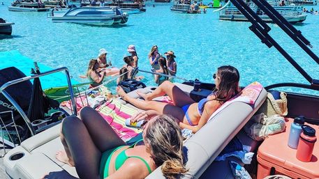 Summer boat party: people sunbathing on a pontoon with anchored boats and swimmers in crystal-clear turquoise water