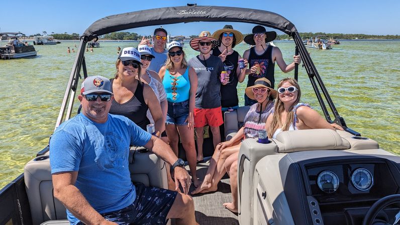 Friends on a pontoon boat at a shallow sandbar in clear turquoise water on a sunny beach day, wearing hats, sunglasses and swimwear.