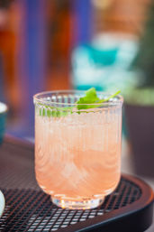 Pink grapefruit cocktail with crushed ice and a mint sprig in a ribbed glass on an outdoor cafe table