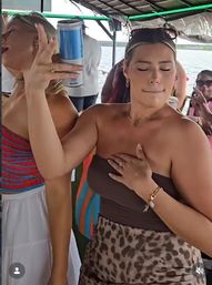 Lively summer boat party on the water with friends — woman in a strapless top and leopard-print skirt holds a can and touches her chest, sunglasses on her head, others dancing and laughing nearby.