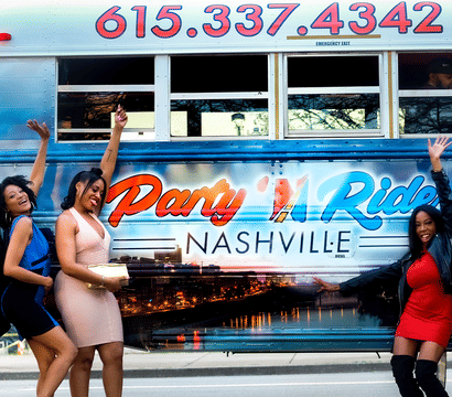 Three women in party dresses cheer and pose beside a colorful Nashville party bus decorated with skyline graphics and bright lettering at a city curb.
