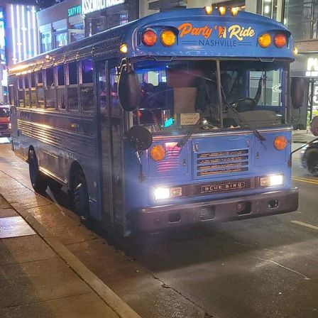 Retro blue party bus parked on a neon-lit downtown Nashville street at night