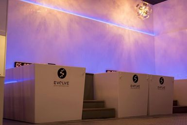 Glowing purple-blue LED-lit wellness studio interior featuring three sleek white recovery pods with digital timers and small step entrances