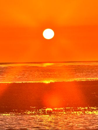 Blazing orange sun setting over the ocean horizon with golden reflections sparkling on rolling waves and wet sand