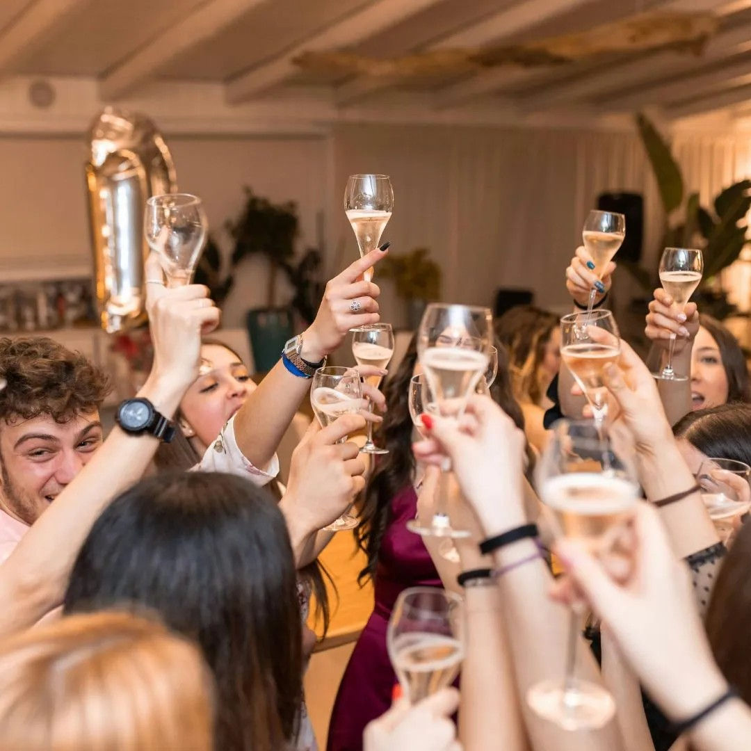 Group toast at an indoor party — people raising champagne flutes in a lively celebration with a metallic balloon in the background