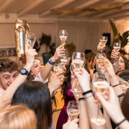 Indoor party scene with a group of people raising champagne flutes in a festive celebratory toast