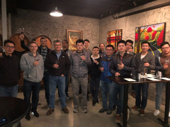 Group of people enjoying a wine tasting in a cozy winery tasting room with wooden barrels and colorful vineyard paintings.