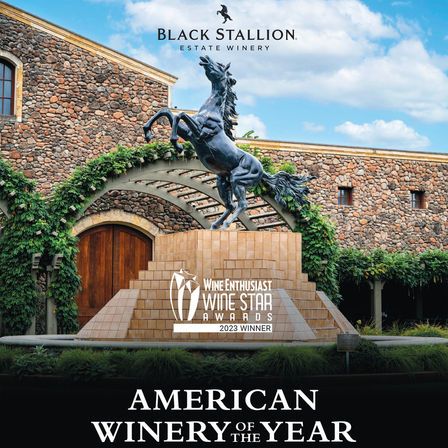 Winery entrance with a rearing horse statue fountain on a tiled pedestal, vine-covered stone façade and an award badge reading "Wine Star Awards 2023 — American Winery of the Year".