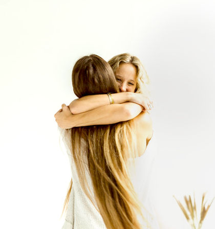 Two women hugging in a bright white room, joyful friendship embrace with long flowing hair