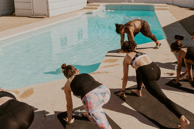 Women practicing poolside yoga on mats by a backyard swimming pool, stretching in lunge poses under bright sun